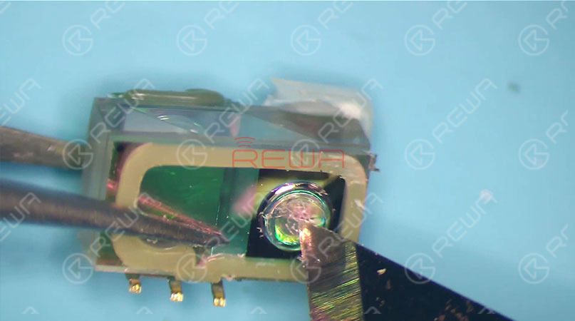 the vulnerabilities of face id: why face id can be easily damaged and hardly repaired? The chip on the left is used to store data, whereas the chip on the right side acts just like a projector. We can see that there are thousands of dots arranged here. The infrared light is emitted from here. Since necessary power supply is needed for chip on the right side to work normally, once water damaged, circuits here are most likely to get short. Which can also result in Face ID not working. And please be noted that the chip is exposed without black adhesive seal. So it can be easily damaged once water-damaged or dropped. What’s more, it also can not be restored once damaged. And this is the internal structure of the dot projector. Let’s continue with the crystal part of the dot projector.