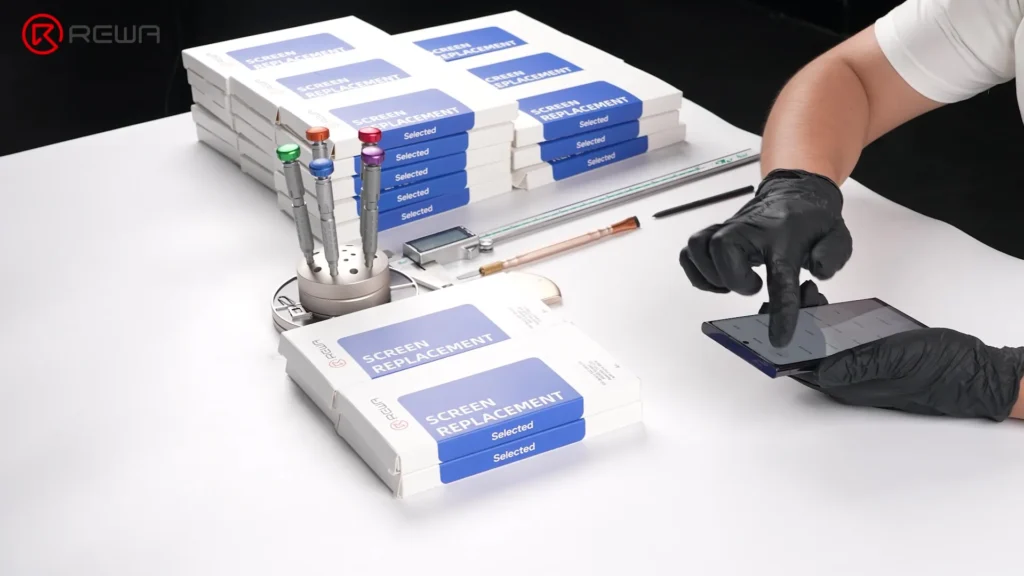 la evolución de las pantallas de repuesto Samsung: de LCD In-cell a OLED avanzados 1:1 Técnico probando la pantalla de un smartphone junto a pilas de cajas de repuesto de pantallas REWA y herramientas de reparación