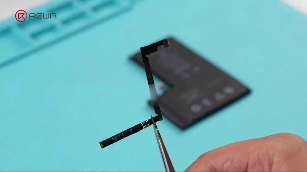 Ein dünnes, schwarzes L-förmiges Batteriemanagementsystem (BMS), das mit einer Pinzette gehalten wird