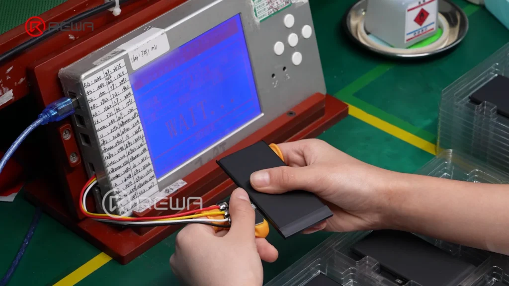 Technician connecting an assembled iPhone battery to a digital testing device to monitor voltage and internal resistance