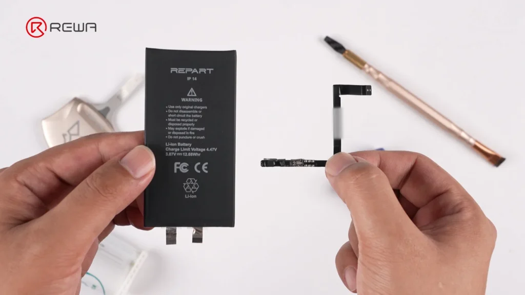 Hands holding a black iPhone 14 battery cell on the left and a small BMS board with flex cable on the right